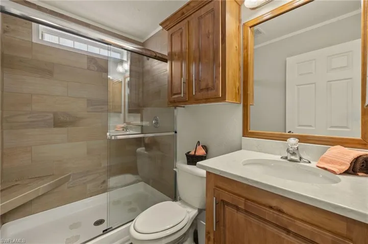 Bathroom with vanity, a shower with shower door, toilet, and ornamental molding
