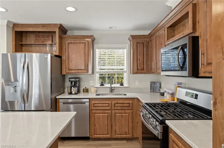 Kitchen with appliances with stainless steel finishes, light hardwood / wood-style flooring, sink, and crown molding