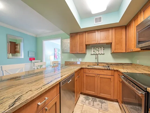 Kitchen featuring light stone counters, appliances with stainless steel finishes, a sink, and visible vents