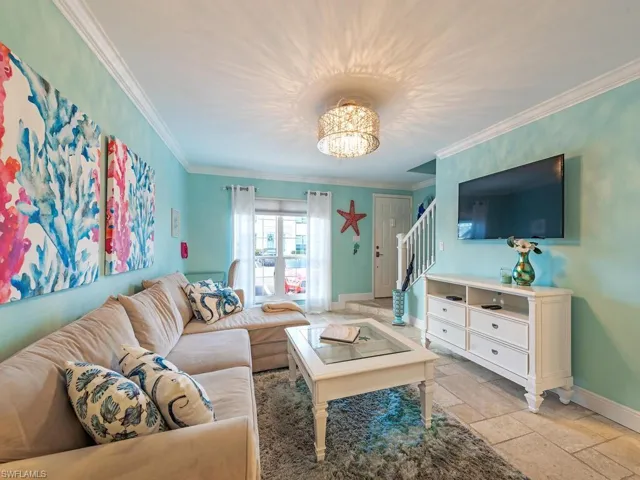 Living area featuring stone tile floors, stairs, baseboards, and ornamental molding