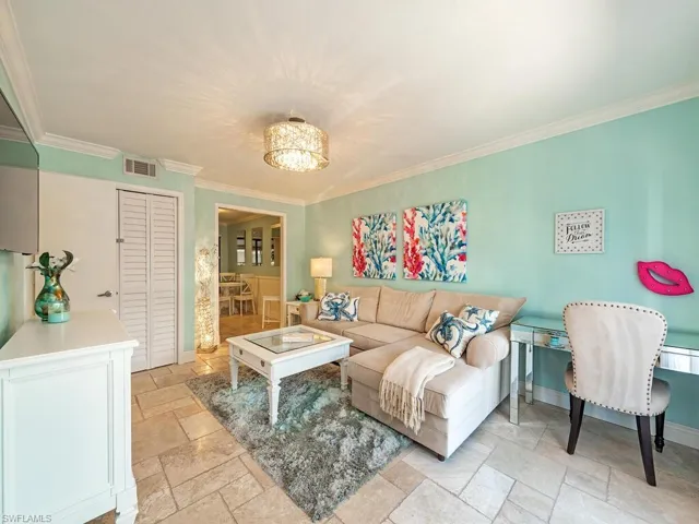 Living area featuring a notable chandelier, visible vents, baseboards, stone tile flooring, and crown molding