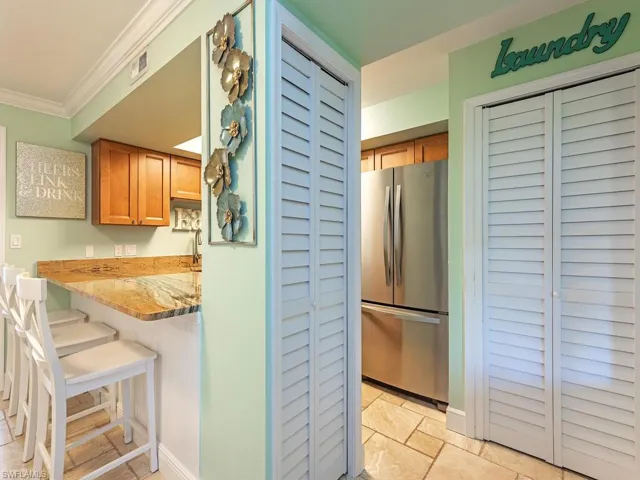 Kitchen featuring visible vents, ornamental molding, a breakfast bar, freestanding refrigerator, and light stone countertops