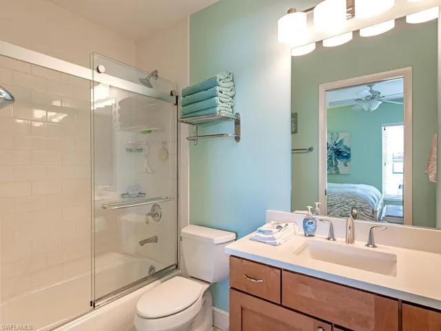 Bathroom featuring toilet, combined bath / shower with glass door, ceiling fan, vanity, and ensuite bath