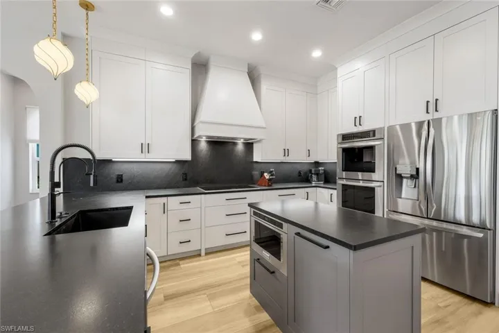Kitchen with stainless steel appliances, custom exhaust hood, white cabinets, and recessed lighting