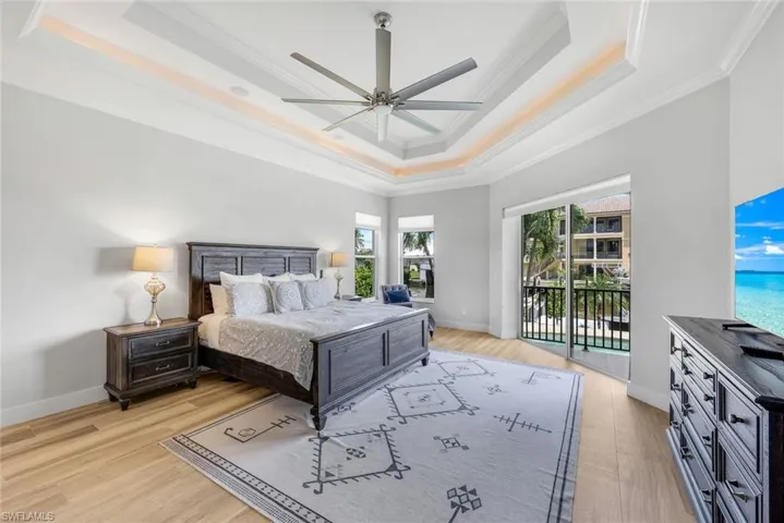 Bedroom with a tray ceiling, ornamental molding, light wood-style floors, access to outside, and a ceiling fan
