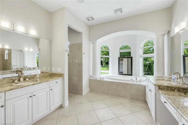 Full bathroom featuring two vanities, a garden tub, a tile shower, and light tile patterned floors