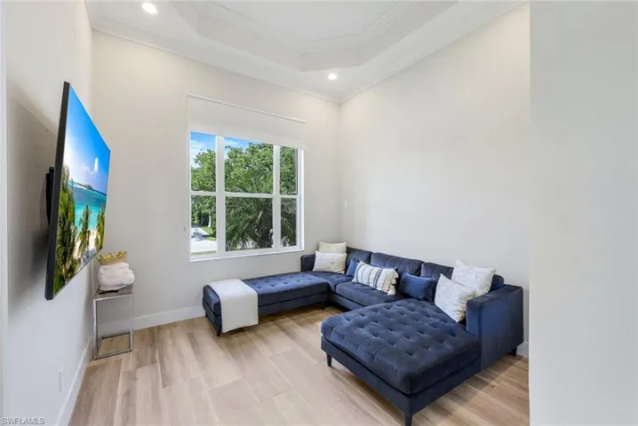 Living room with crown molding, a tray ceiling, light wood-style floors, and recessed lighting