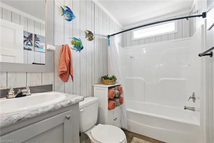 Full bath with shower / bath combo with shower curtain, toilet, vanity, a textured ceiling, and wooden walls