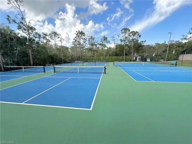 View of tennis court featuring community basketball court and view of wooded area