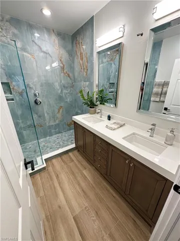 Full bath with a marble finish shower, double vanity, wood finish floors, and recessed lighting