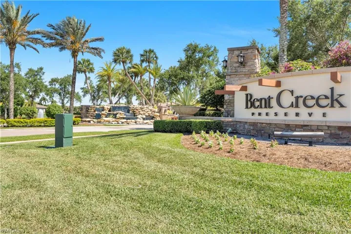 Stone-clad entry monument for Bent Creek Preserve featuring established landscaping, a decorative water feature, and mature palm trees