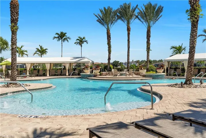 Expansive pool area featuring a freeform swimming pool with integrated spa, paver deck, and multiple shaded cabanas