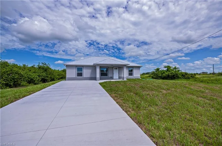 View of front of property featuring a standing seam roof, metal roof, driveway, and stucco siding