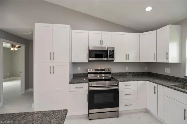 Kitchen featuring white cabinets, lofted ceiling, appliances with stainless steel finishes, dark stone countertops, and marble finish floor