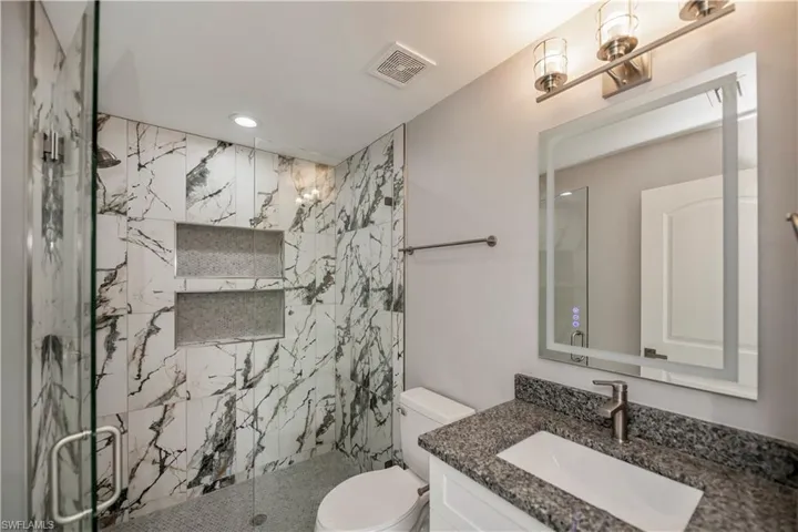 Full bath featuring toilet, recessed lighting, vanity, visible vents, and a marble finish shower