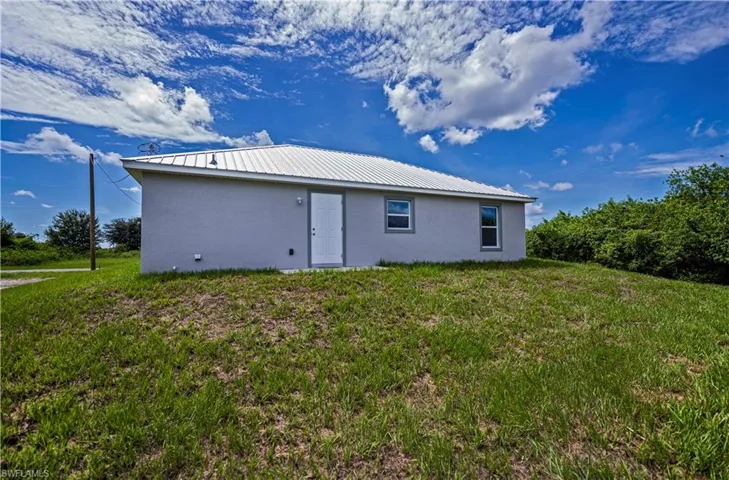Back of property featuring metal roof, a lawn, and stucco siding