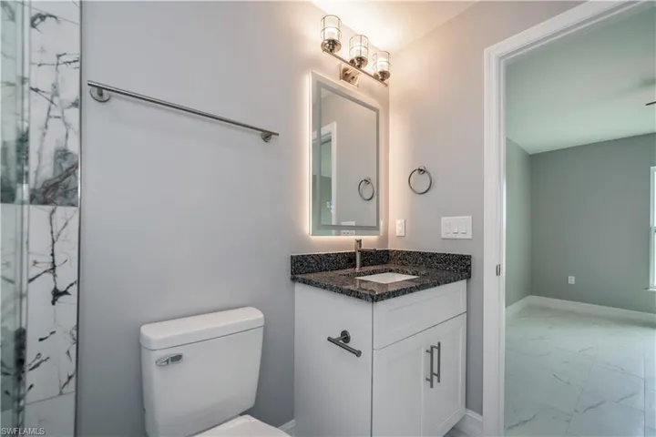 Bathroom with a marble finish shower, baseboards, toilet, marble finish floor, and vanity