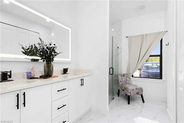 Bathroom featuring marble finish floors, a marble finish shower, baseboards, and double vanity