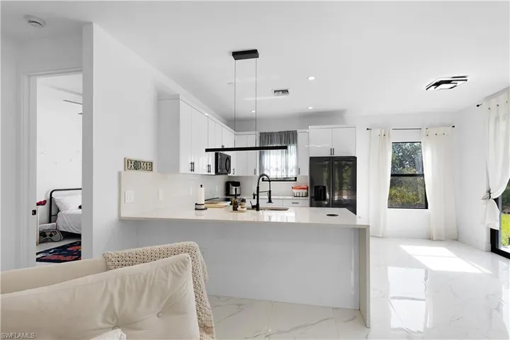 Kitchen featuring black appliances, a sink, light countertops, a peninsula, and white cabinetry