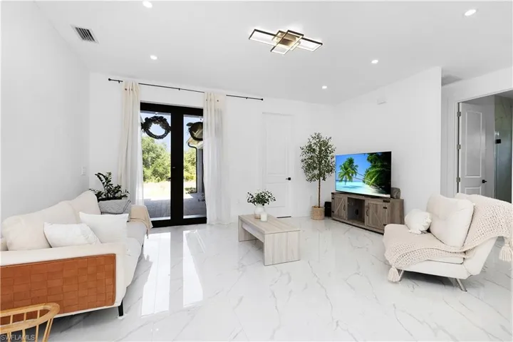 Living room featuring light marble finish flooring, recessed lighting, and french doors