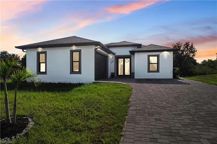 View of front facade featuring an attached garage, stucco siding, french doors, a front yard, and decorative driveway