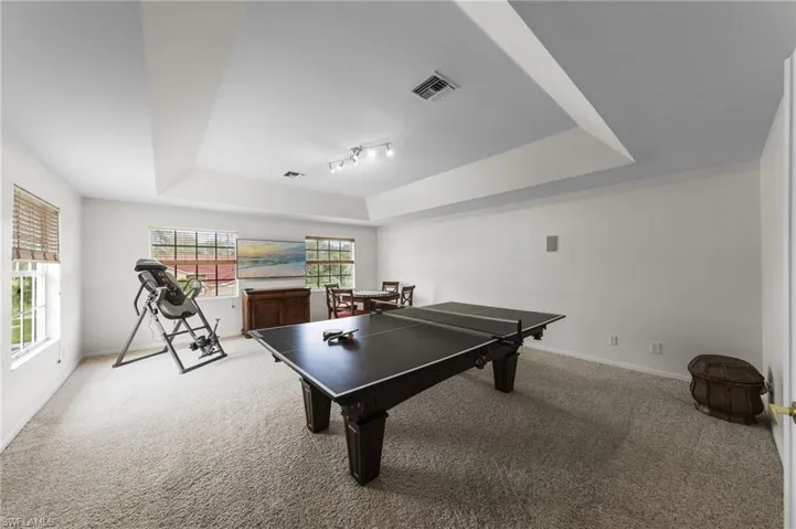 Carpeted room featuring a tray ceiling, recessed lighting, and multiple windows with blinds