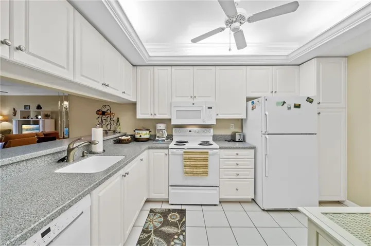 Kitchen featuring white appliances, light tile patterned floors, white cabinets, ornamental molding, and a ceiling fan