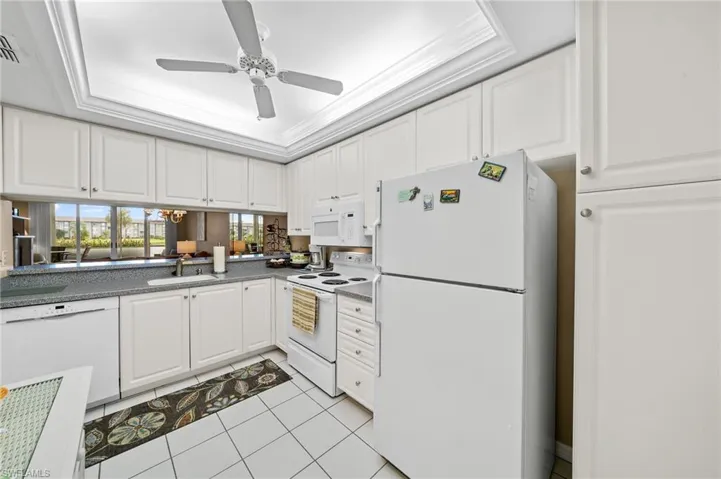 Kitchen featuring a raised ceiling, white cabinetry, white appliances, light tile patterned floors, and crown molding