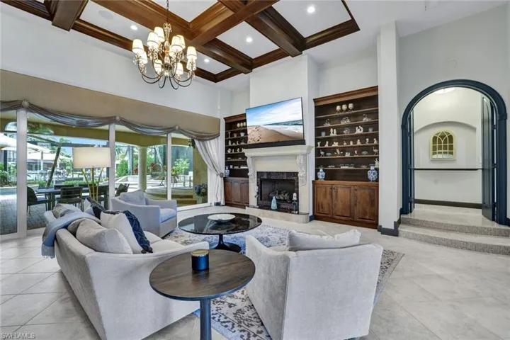 Tiled Great Room with a fireplace, chandelier, and high coffered ceiling, entry to Master Bedroom on right.