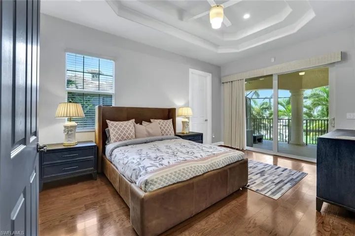 5th Bedroom with a raised tray ceiling, hardwood flooring, ensuite bathroom, and access to screened balcony overlooking the pool and lanai.