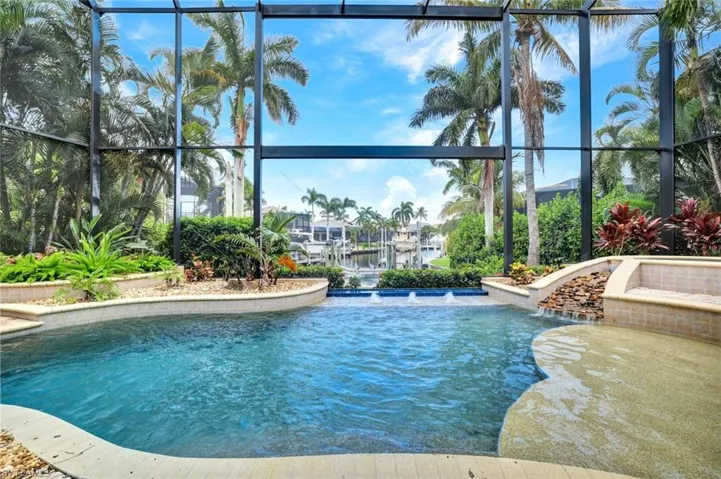 Large infinity edge pool with SW rear exposure, custom water features, sun shelf, integrated spa and waterfall, and in pool table top with seating area (to the left of this view closer to the summer kitchen).