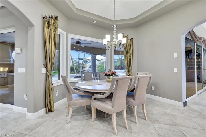 Tiled dining space featuring chandelier, tray ceiling and bay windows overlooking that lanai and pool area.