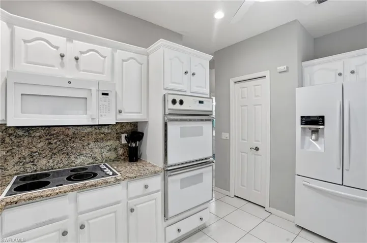 Kitchen with white appliances, white cabinetry, light tile patterned flooring, tasteful backsplash, and light stone countertops