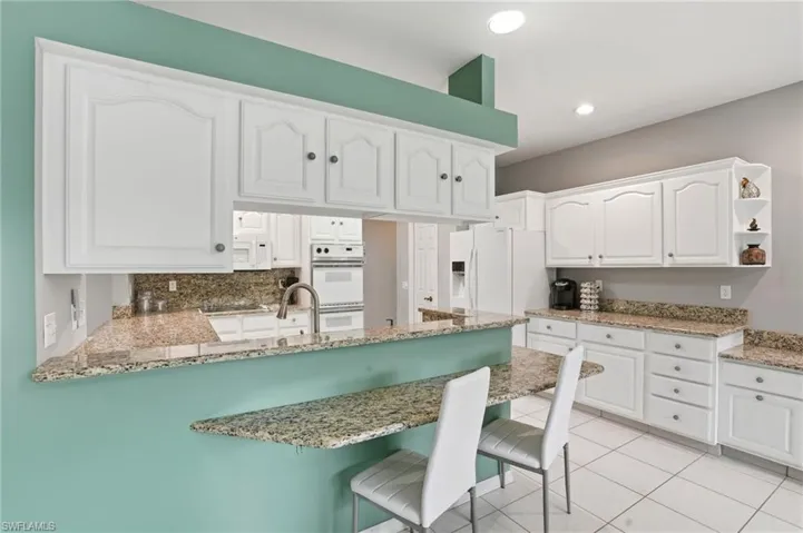 Kitchen featuring white cabinetry, light stone countertops, a peninsula, a breakfast bar, and white appliances