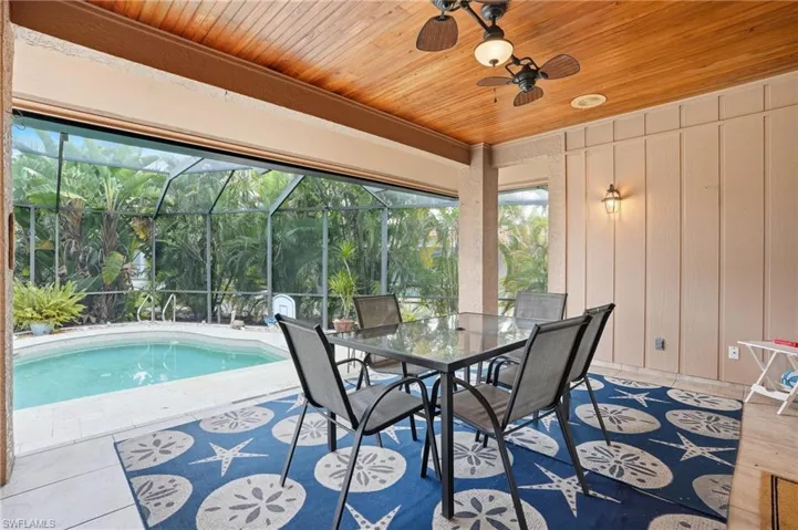 Sunroom with outdoor dining area, ceiling fan, a patio, and a pool