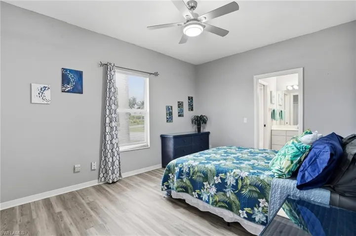 Bedroom with light wood-style floors, ceiling fan, and ensuite bath