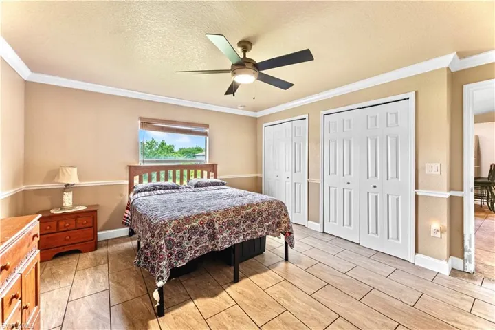 Tiled bedroom featuring multiple closets, a textured ceiling, crown molding, and ceiling fan