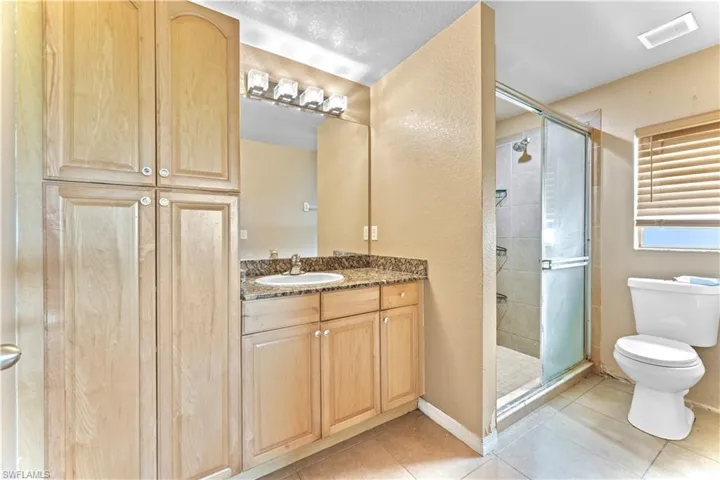 Bathroom featuring tile patterned flooring, a shower with door, toilet, and vanity
