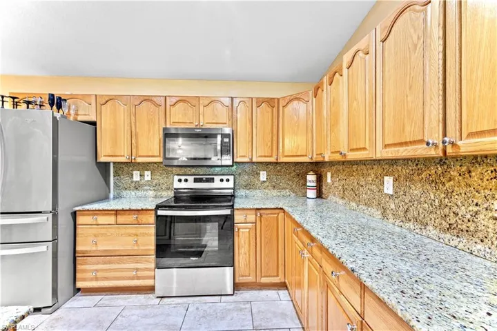 Kitchen featuring light tile patterned flooring, light stone counters, backsplash, and stainless steel appliances