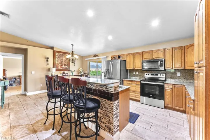 Kitchen featuring stainless steel appliances, vaulted ceiling, decorative backsplash, a kitchen island with sink, and light tile patterned flooring