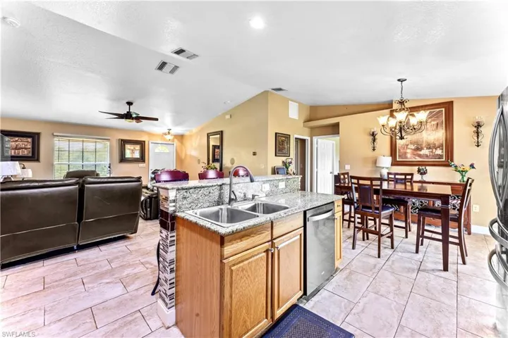 Kitchen featuring stainless steel dishwasher, ceiling fan with notable chandelier, an island with sink, lofted ceiling, and light tile patterned floors