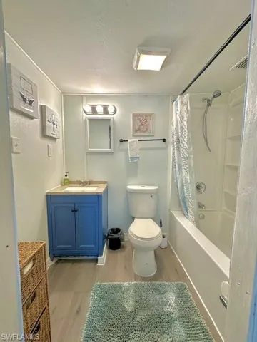 Bathroom featuring wood finished floors, toilet, vanity, shower / bath combo with shower curtain, and a textured ceiling