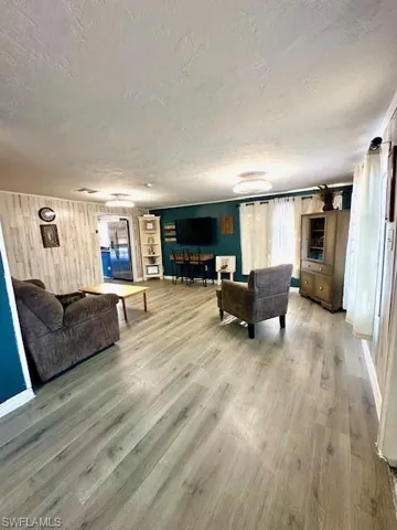 Living room with a textured ceiling, light wood finished floors, and wooden walls