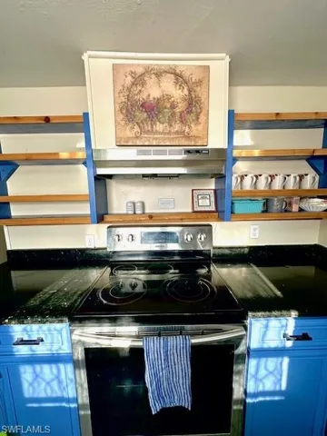Kitchen view of electric stove, under cabinet range hood, and dark countertops
