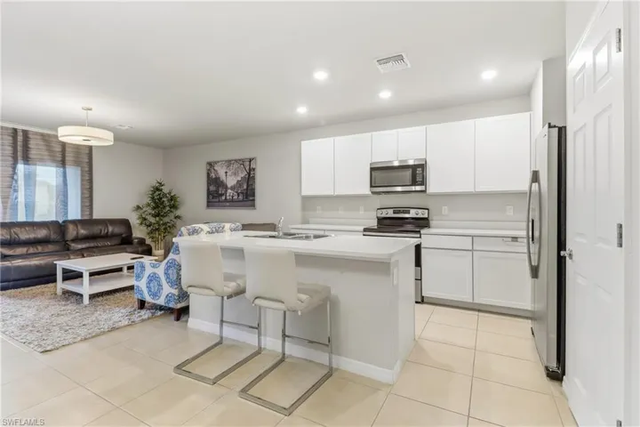 Kitchen with a kitchen breakfast bar, appliances with stainless steel finishes, white cabinetry, a kitchen island with sink, and recessed lighting