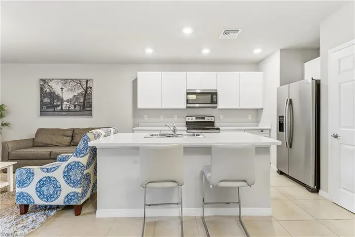 Kitchen with stainless steel appliances, light countertops, a breakfast bar area, a center island with sink, and recessed lighting