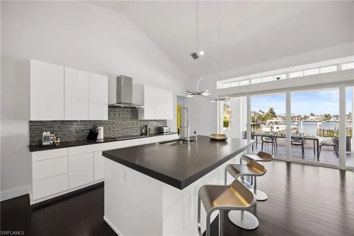 Kitchen with high vaulted ceiling, a breakfast bar area, an island with sink, modern cabinets, and white cabinetry