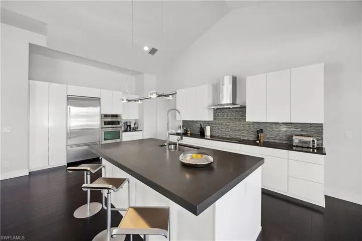 Kitchen with high vaulted ceiling, decorative backsplash, stainless steel appliances, a kitchen breakfast bar, and modern cabinets