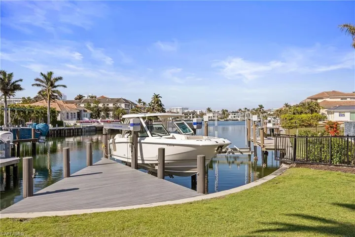 Dock featuring boat lift, a water view, a lawn, and a residential view