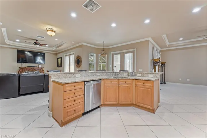 Kitchen with stainless steel dishwasher, a kitchen island with sink, sink, and light stone counters